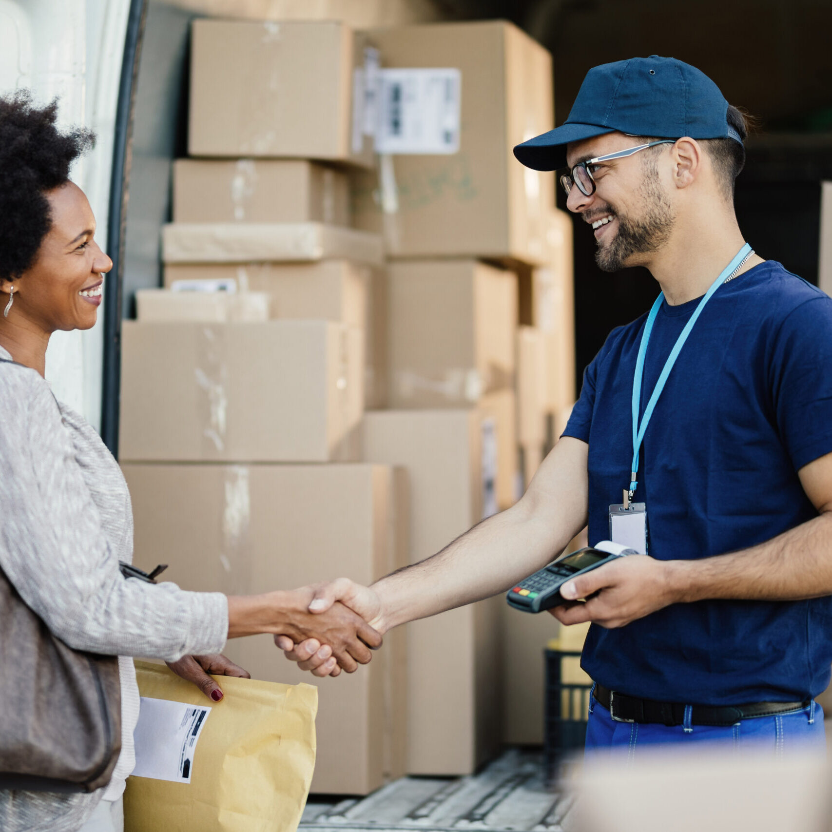 African American woman shaking hands with delivery man while rec Happy courier handshaking with African American woman while delivering her a package.